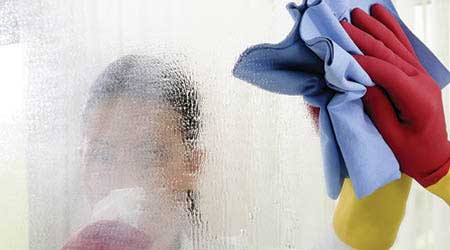woman cleaning mirror with chemical and microfiber cloth