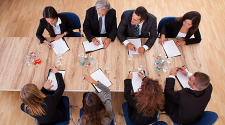 Overhead view of a group of professional business people in a meeting seated around a wooden table with their notepads