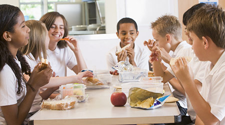 Students sitting at cafeteria table eating lunch