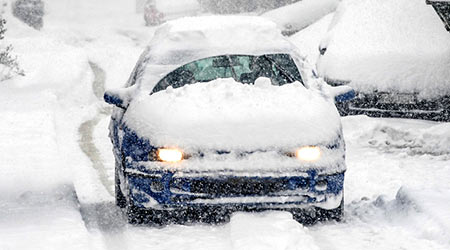 A snow covered car drives in winter storm
