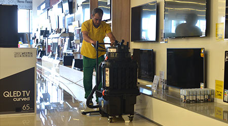Man pushes walk-behind floor equipment to clean and shine the floors inside a retail store