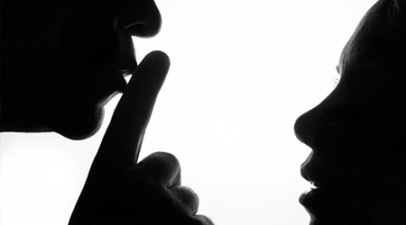 Man holding finger in front of his mouth to signal woman not to say anything