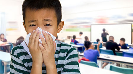 Kid at school blowing his nose with a tissue