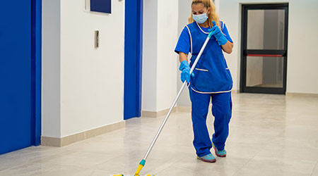 A cleaning lady with a mask on her face cleans the hallway