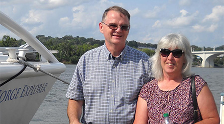 older man in sunglasses standing next to an older woman and a boat