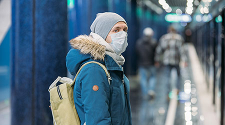 Ill young man feeling sick, wearing protective mask against transmissible infectious diseases and as protection against the flu in public and transportation.