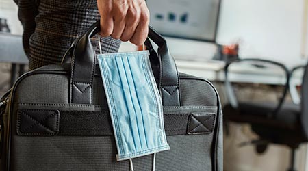 closeup of a young man in an office holding a briefcase and a surgical mask in his hand