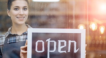 Femal owner of a small business flips the sign at the entrance of her store to open