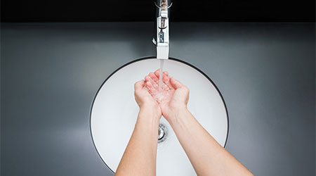 Young woman washing hands under the water tap. Water running. White, modern ceramic sink with dark gray table surface. Daily hygiene. Point of view shot. Contemporary restroom. Part of body.