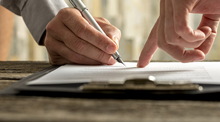 Closeup of businessman showing his new business partner where to sign an agreement or contract with fountain pen on rustic wooden desk.