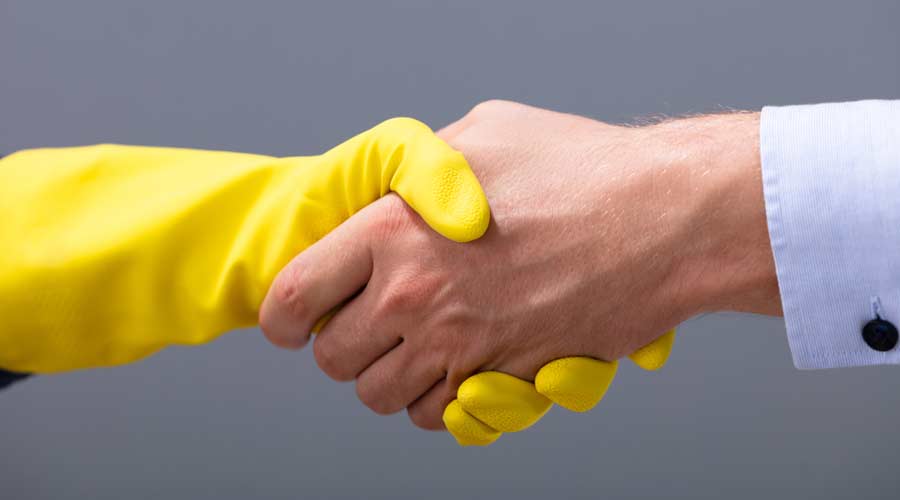 Close-up Of Businessman And Janitor Shaking Hands Together Against Gray Background