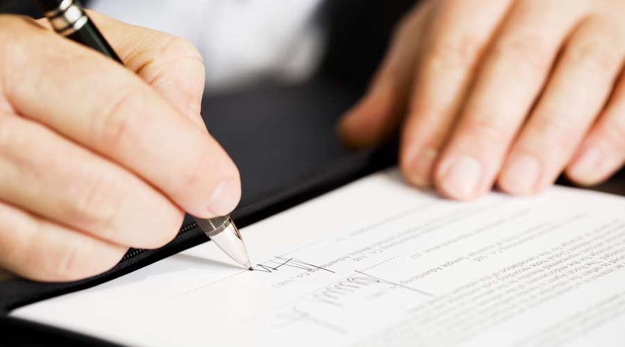 Businessman sitting at office desk signing a contract with shallow focus on signature.