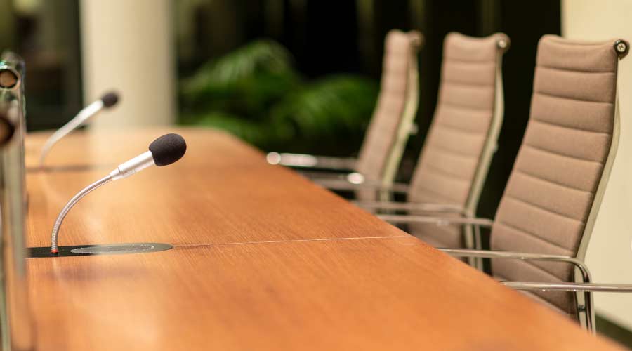 Isolated view of a microphone in a meeting room on a table with blurred chairs - close-up with selective focus, very little depth of field and much copyspace