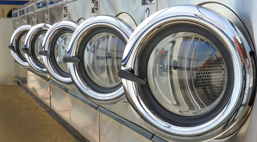 Row of industrial laundry machines in laundromat.