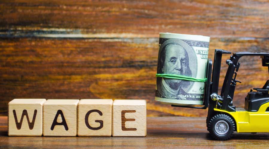 Wooden blocks with the word Wage, dollars and a forklift. Financial compensation. Salary payment to employees. Minimum and nominal wages rates. Profit and income. Business and finance