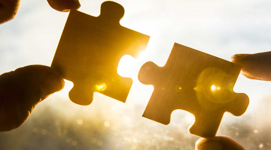 two hands trying to connect couple puzzle piece with sunset background. Jigsaw alone wooden puzzle against sun rays. one part of whole. symbol of association and connection. business strategy.