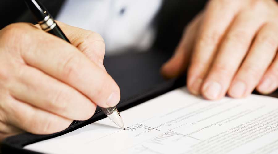 Businessman sitting at office desk signing a contract with shallow focus on signature.