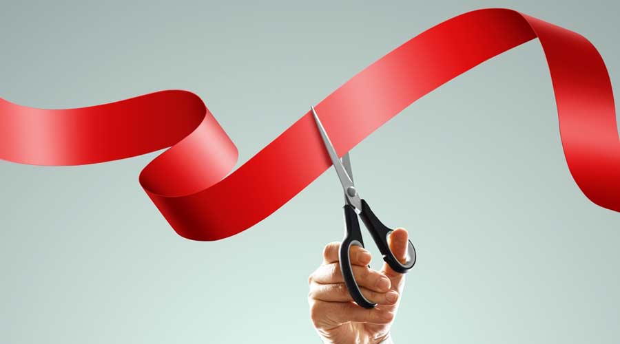 Grand opening with red ribbon and scissors. A businessman's hand holds scissors cuts a red ribbon on a light background. Close-up, copy space