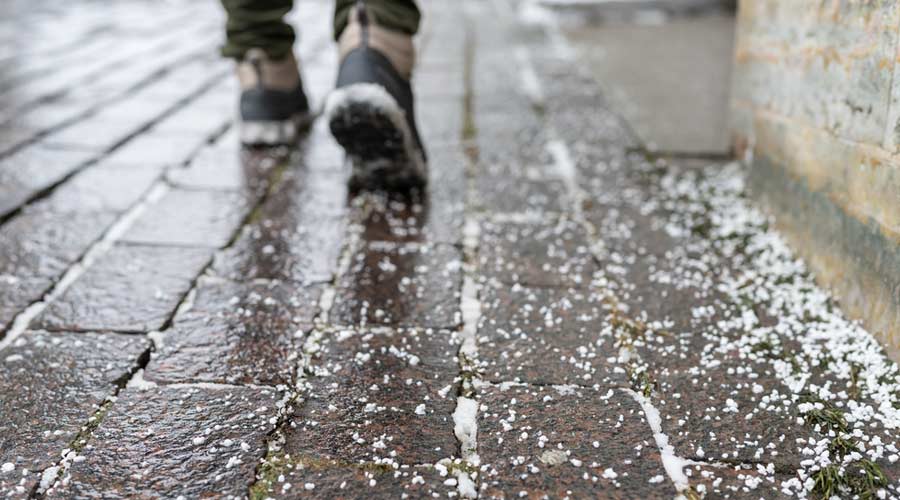 Selective focus on technical salt grains on icy sidewalk surface in wintertime, used for melting ice and snow. Applying salt to keep roads clear and people safe in winter weather from ice or snow