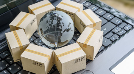 International freight or shipping service for online shopping or ecommerce concept : Paper boxes or carton put in circle around a clear crystal globe with world map on a computer notebook keyboard.