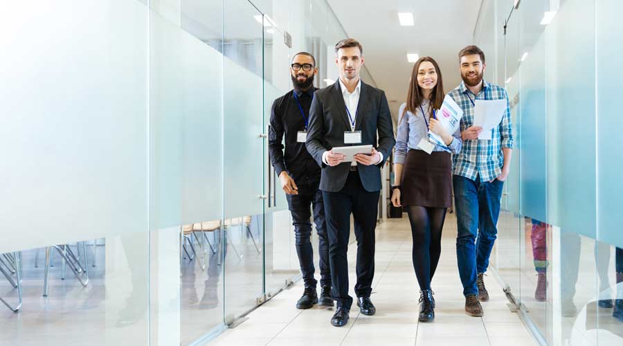 Full length of group of happy young business people walking the corridor in office together