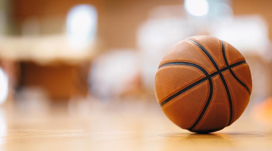Close-up image of basketball ball over the floor in the gym. Orange basketball ball on wooden parquet.