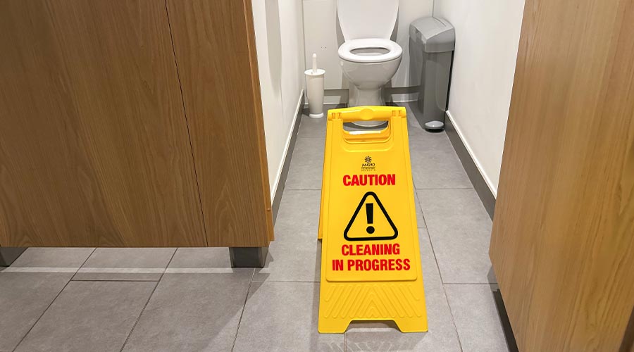 Caution cleaning in progress sign is prominently displayed in a restroom, next to a toilet and waste bin, highlighting maintenance efforts in a public space