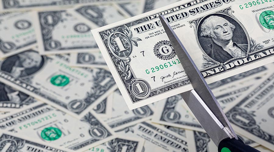 Scissors cutting a one dollar bill, cash money. Inflation, budget cuts and cost cutting concept