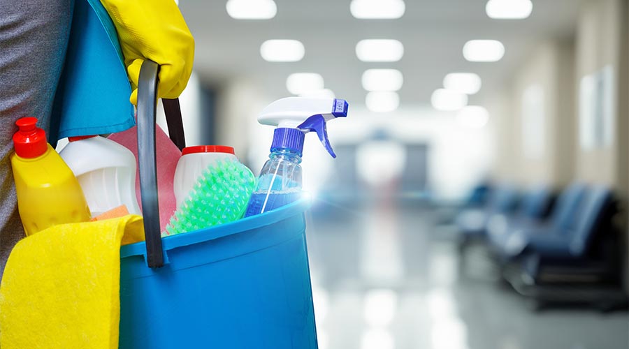 Cleaning woman with bucket and cleaning supplies on blurred background of hospital or office corridor