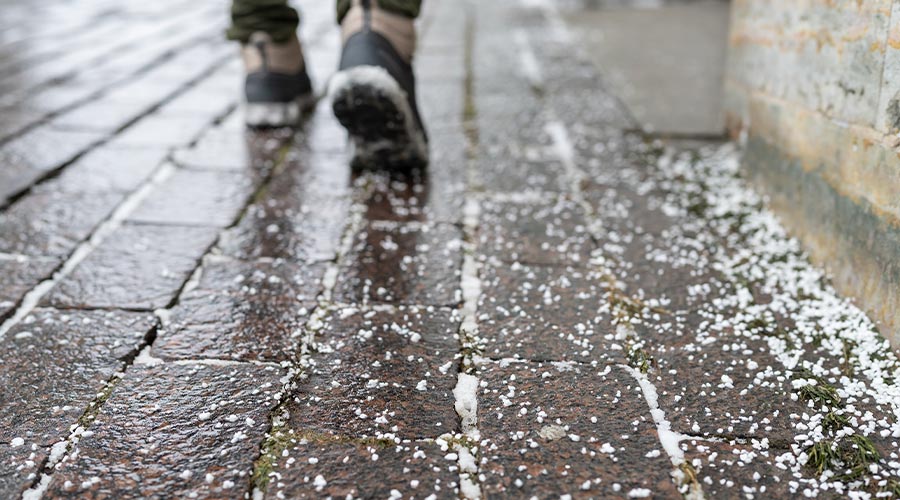 Selective focus on technical salt grains on icy sidewalk surface in wintertime, used for melting ice and snow. Applying salt to keep roads clear and people safe in winter weather from ice or snow