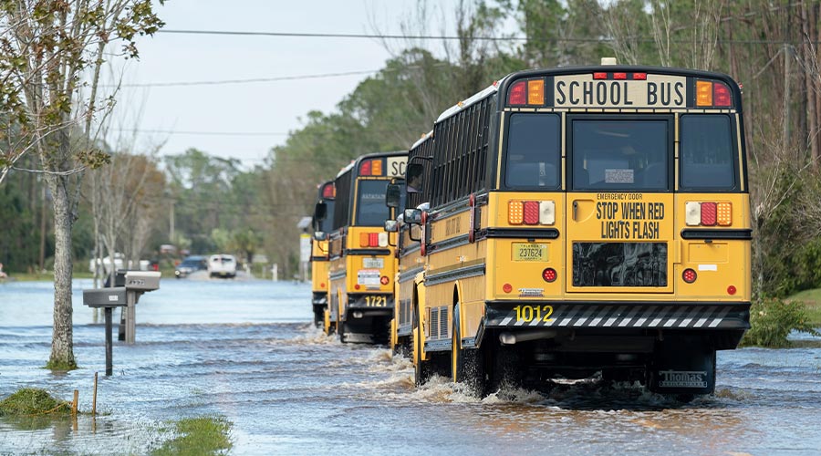 Hurricane Ian flooded street with moving evacuation school buses in surrounded with water Florida residential area. Consequences of natural disaster. Fort Myers, USA