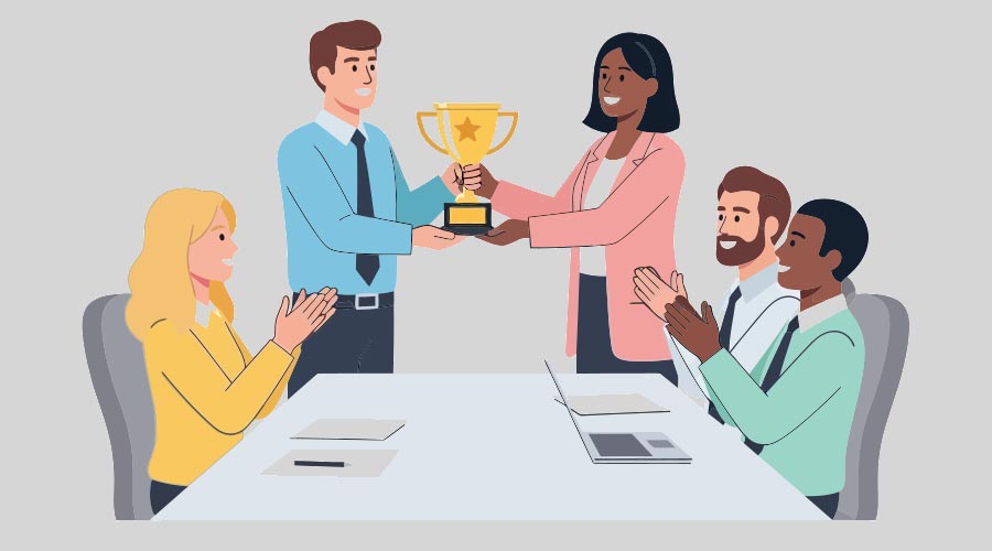 A group of smiling, diverse colleagues at a conference table, with a woman awarding a gold trophy to a man as others applaud their professional achievement
