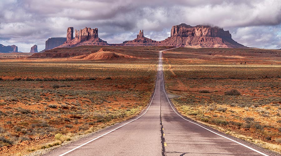View of Forrest Gump Scenic road in Monument Valley, Utah during a cloudy day shows the long, lonely road moving into Arizona through the famous mountain range shown in the movie.