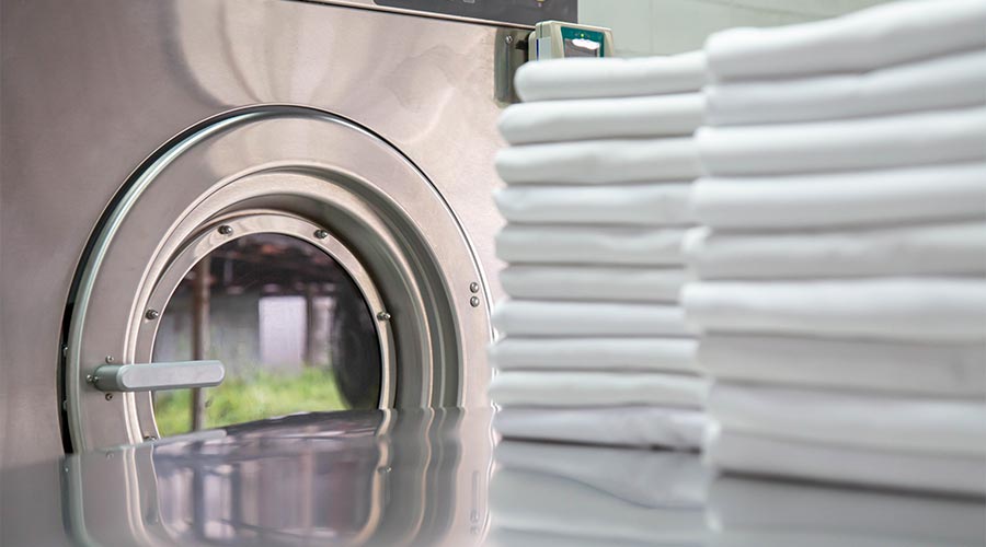 Stack of clean bed sheets in front of industrial washing machine. Focused on washing machines. Shot taken in the factory