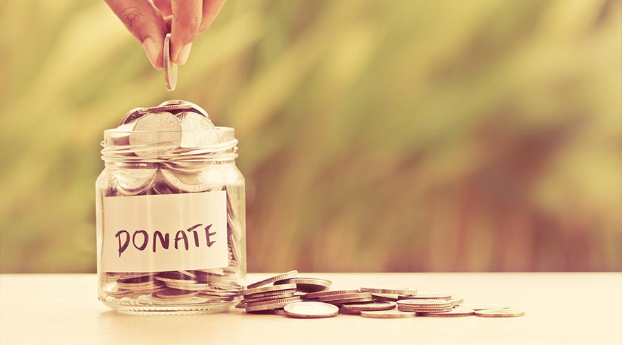 Hand putting Coins in glass jar with DONATE word written text label for giving and donation concept
