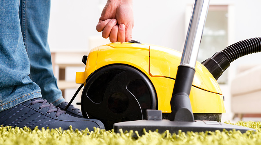 Man cleaning the floor carpet with a vacuum cleaner close up