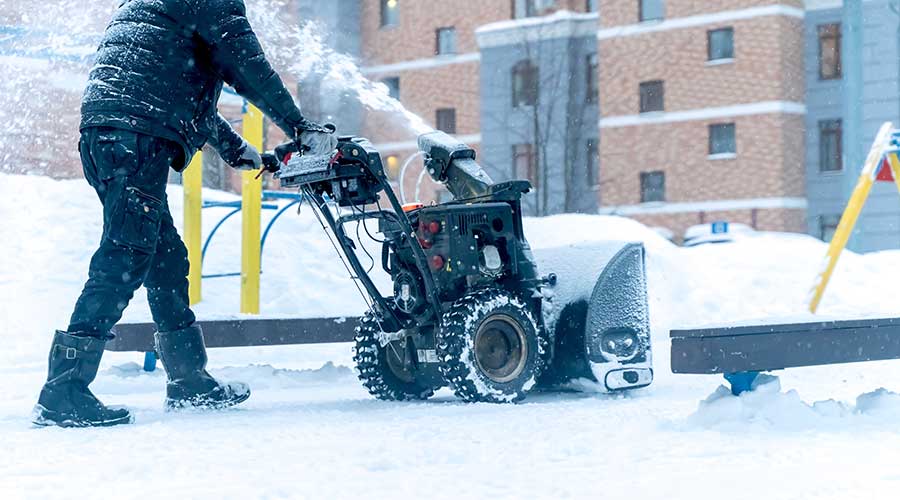 A janitor with a snow blower removes snow in the yard of the house