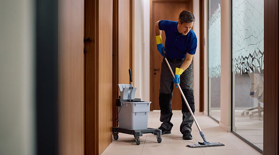 Cleaning staff member mopping corporate office corridor. Copy space. 