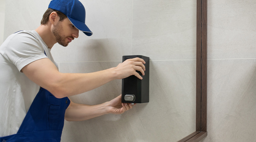 Worker fixing wall mounted soap dispenser in modern bathroom