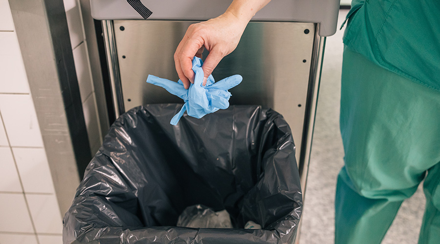 Medical personnel in green scrubs throwing gloves in the garbage