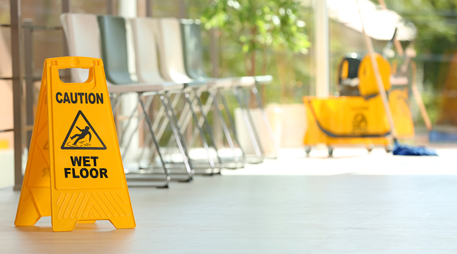 Safety sign with phrase Caution wet floor and blurred mop bucket on background. Cleaning service
