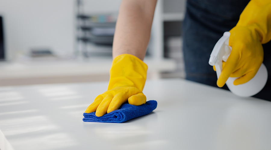 Person cleaning the room, cleaning staff is using cloth and spraying disinfectant to wipe the desk in the company office room. Cleaning staff. Maintaining cleanliness in the organization.